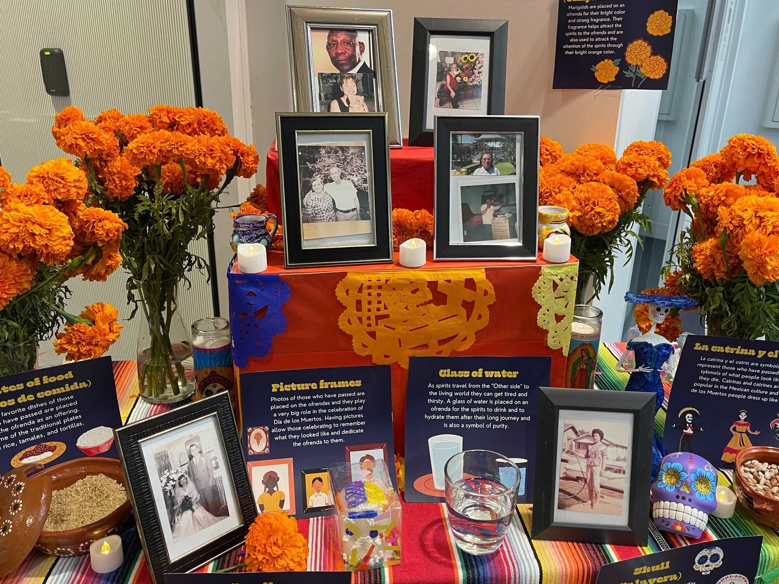 una imagen de una vela encendida y flores colocadas en un altar con fotografias de seres queridos scaled