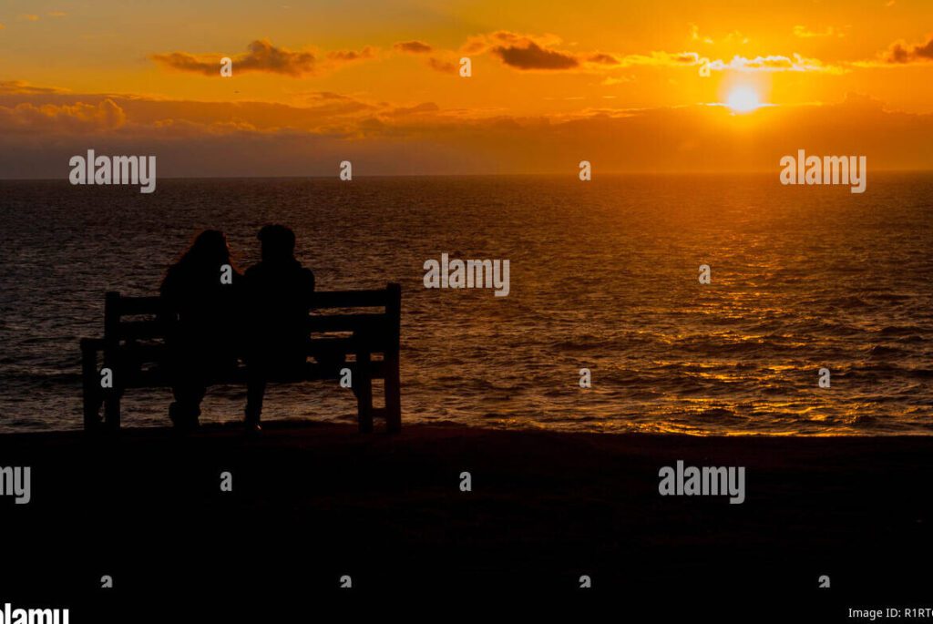 Superando las decisiones no tomadas en el amor: consejos para avanzar 1 una pareja sentada en un banco mirando hacia el horizonte con expresiones serias y reflexivas