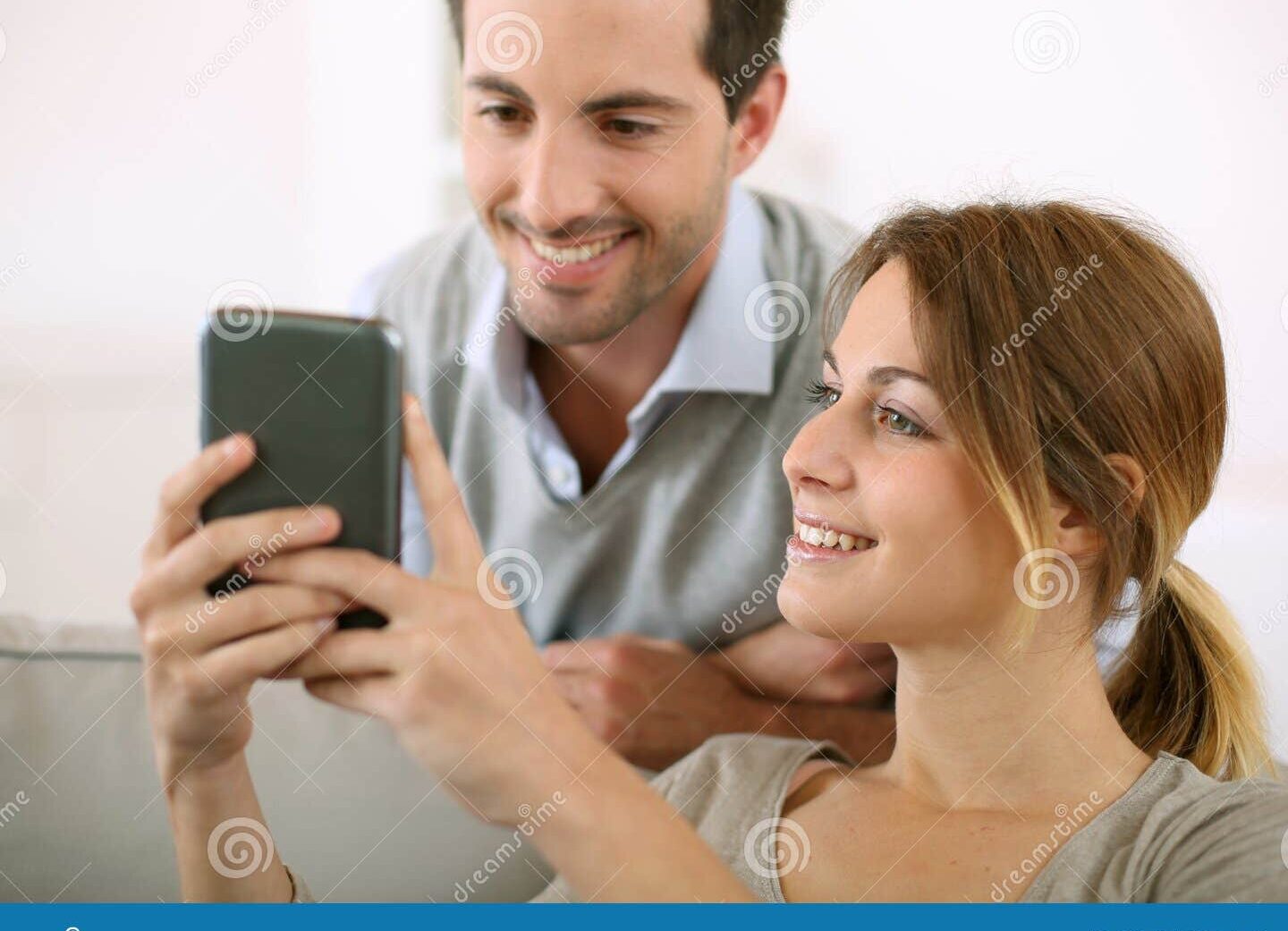 una pareja sonriente enviandose mensajes de amor en sus telefonos moviles